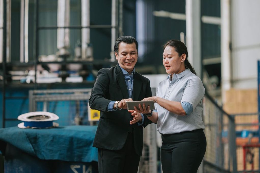 Female foreperson showing businessman factory production and logistics planning on tablet