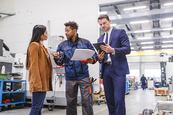 Warehouse worker in uniform discussing year-end inventory with male and female managers, one holding tablet and the other listening attentively