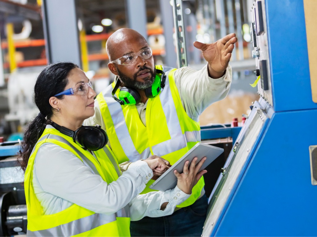 Two factory workers reviewing a machine control panel while navigating a career change.